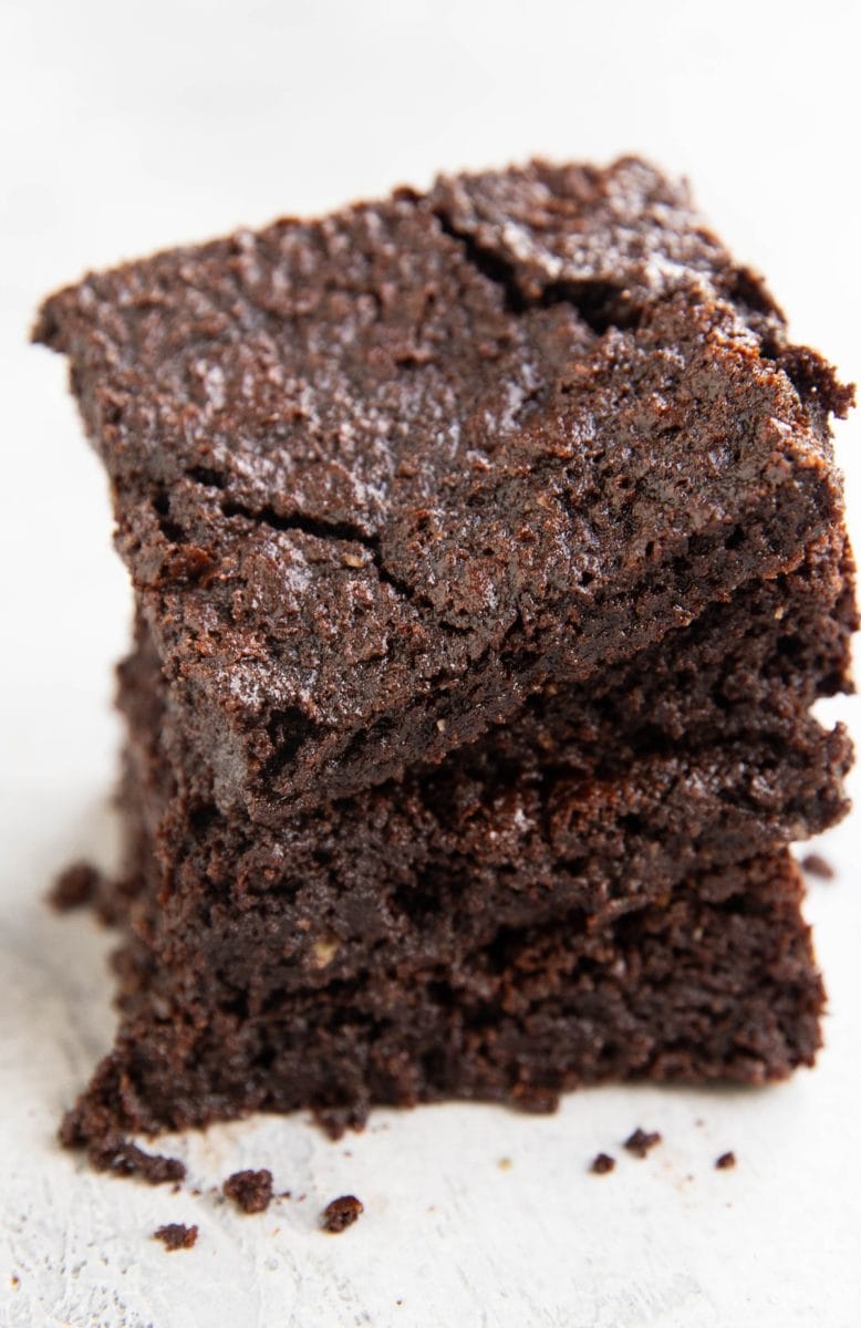 Stack of oat flour brownies on a white background so you can see the crinkle top and the fudgy insides.