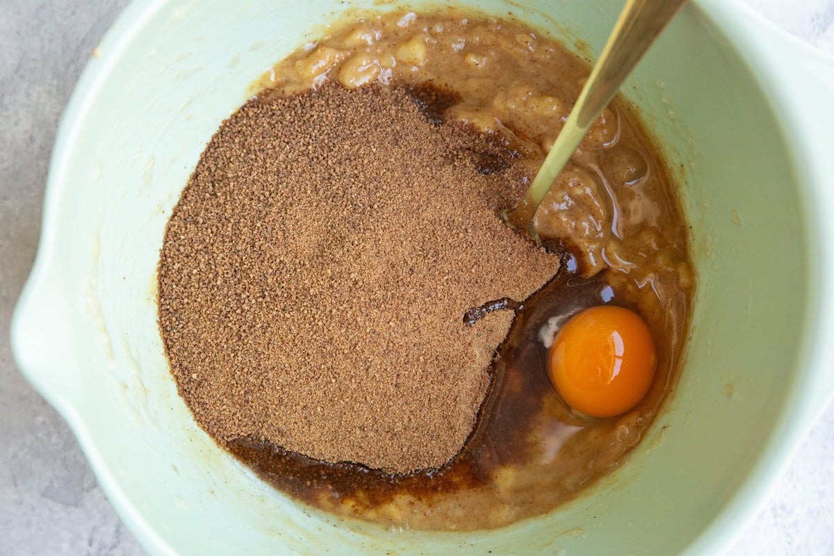 Mixing bowl full of mashed banana and peanut butter with coconut sugar and an egg on top, ready to be mixed in.