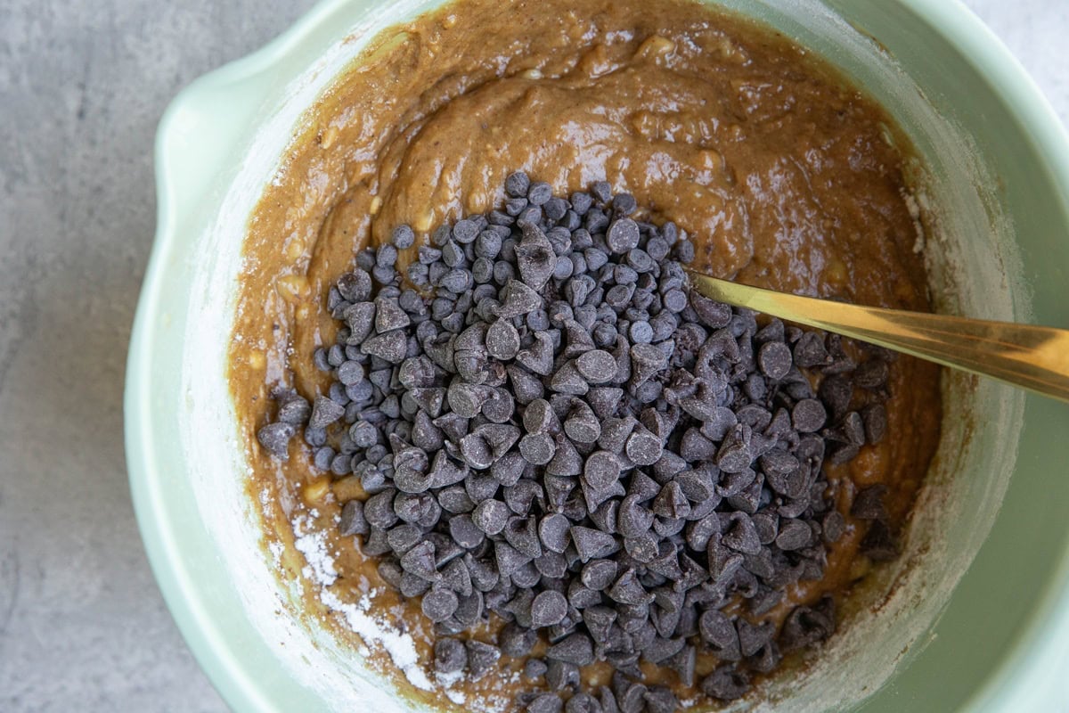 Chocolate chips on top of peanut butter banana bread batter, ready to be mixed in.