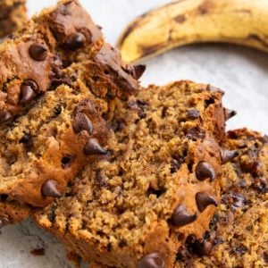 Loaf of peanut butter banana bread cut into slices with a ripe banana in the background.