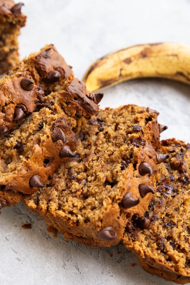 Loaf of peanut butter banana bread cut into slices with a ripe banana in the background.