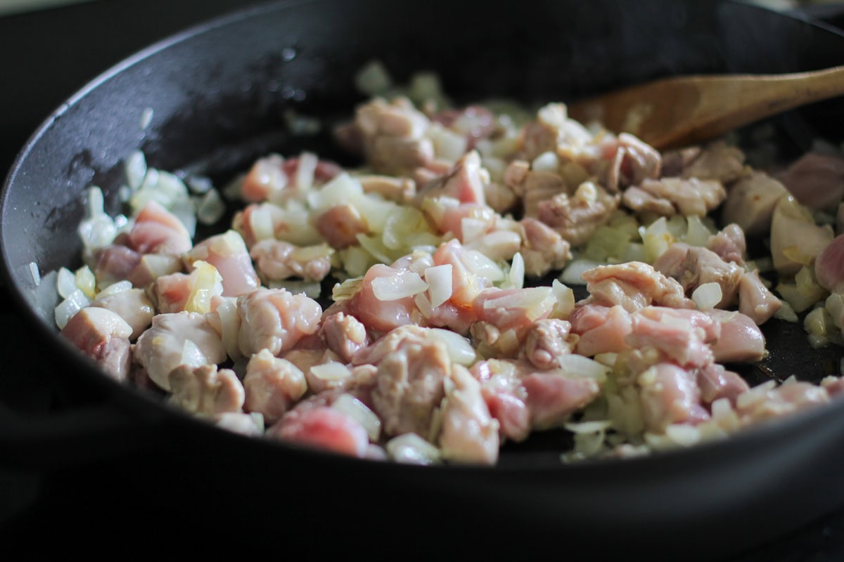 Onion and chopped chicken thighs cooking in a skillet.