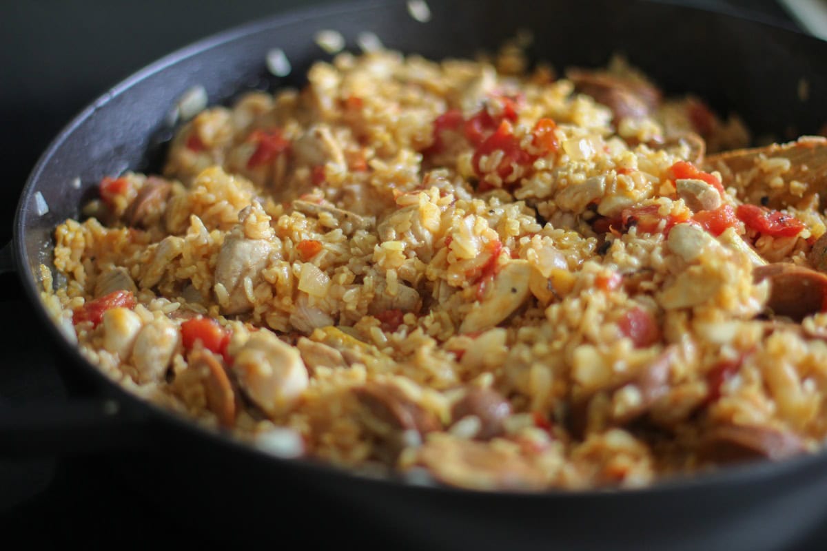 paella pan with rice and meat mixture cooking on the stove top.