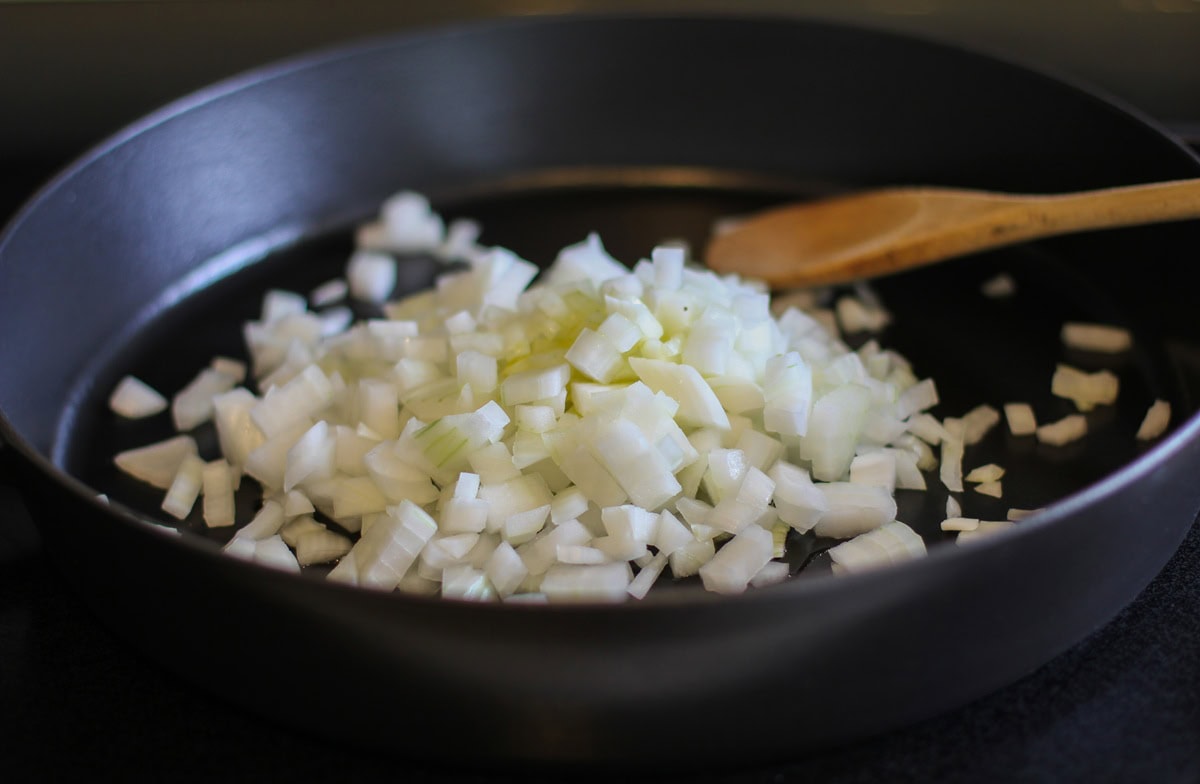 Onion sautéing in a paella pan with a wooden spoon in the background.