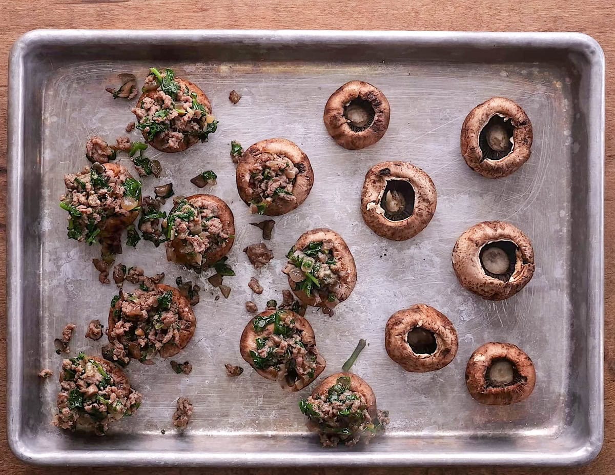Baking sheet with mushrooms turned upside down with the stems removed and meat mixture stuffed in.