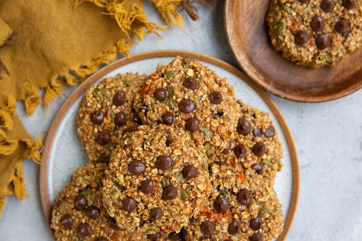 Plate of sweet potato cookies with a wooden plate with one cookie to the side and a golden napkin, ready to serve.