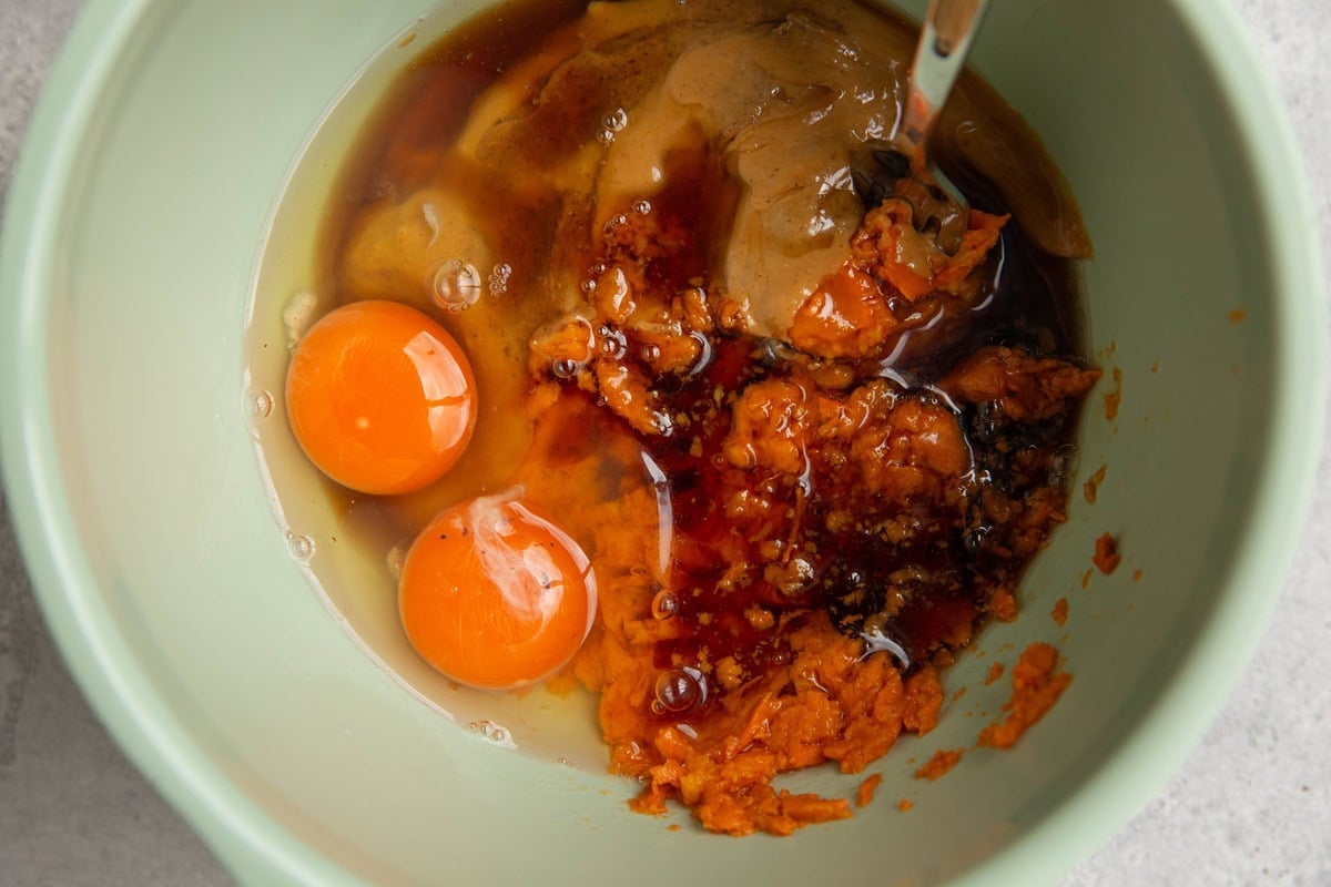 Mixing bowl full of mashed sweet potato, eggs, almond butter, and pure maple syrup, ready to mix together.