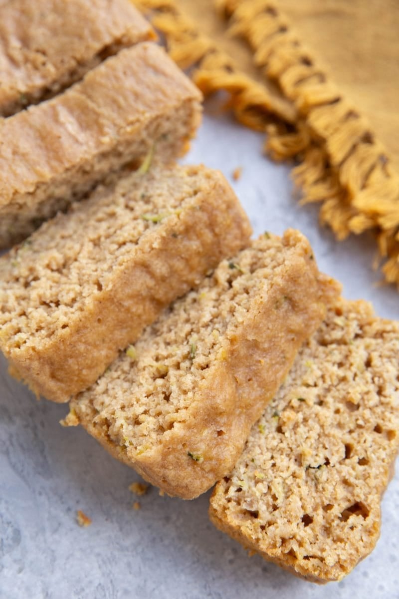 Loaf of yogurt zucchini bread cut into slices with a golden napkin in the background.