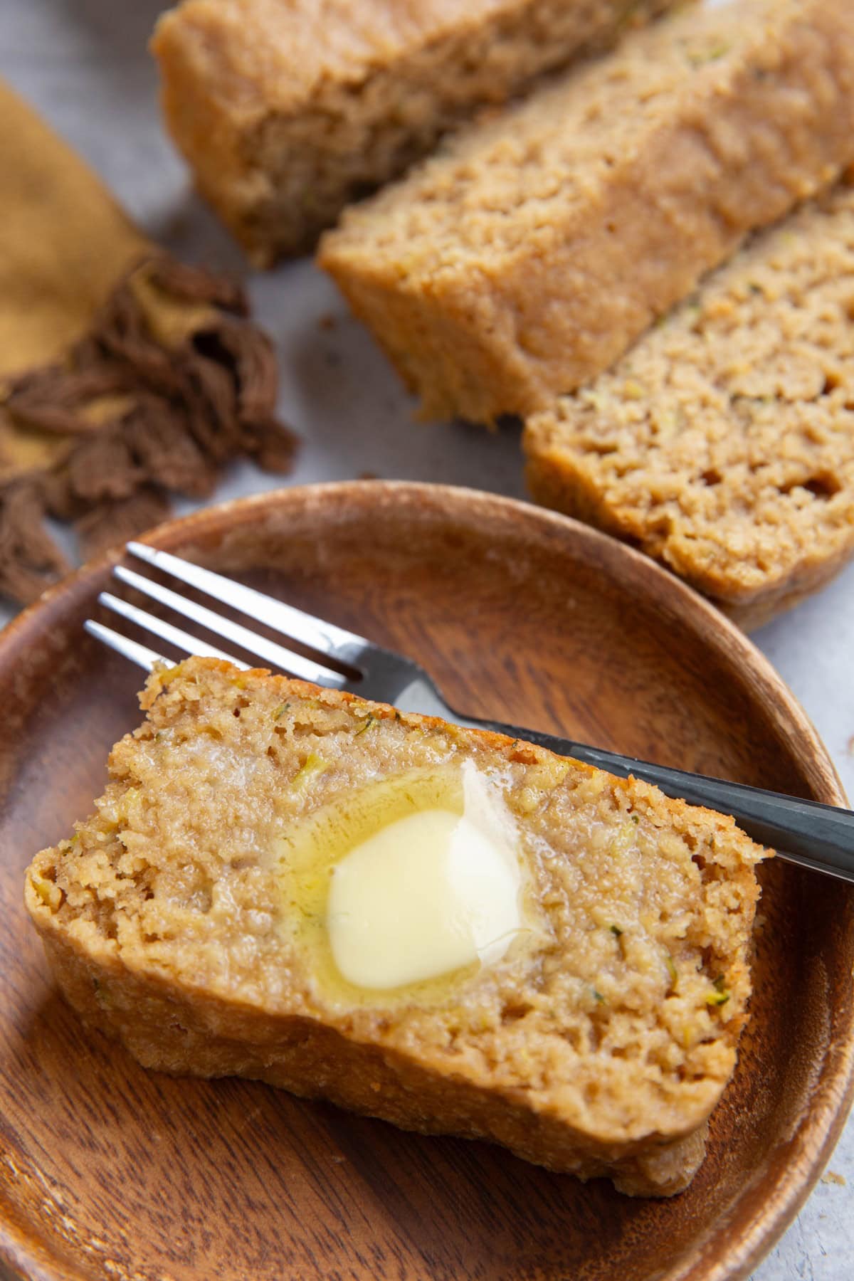 Slice of zucchini bread with melted butter on top with the rest of the loaf sliced in the background.