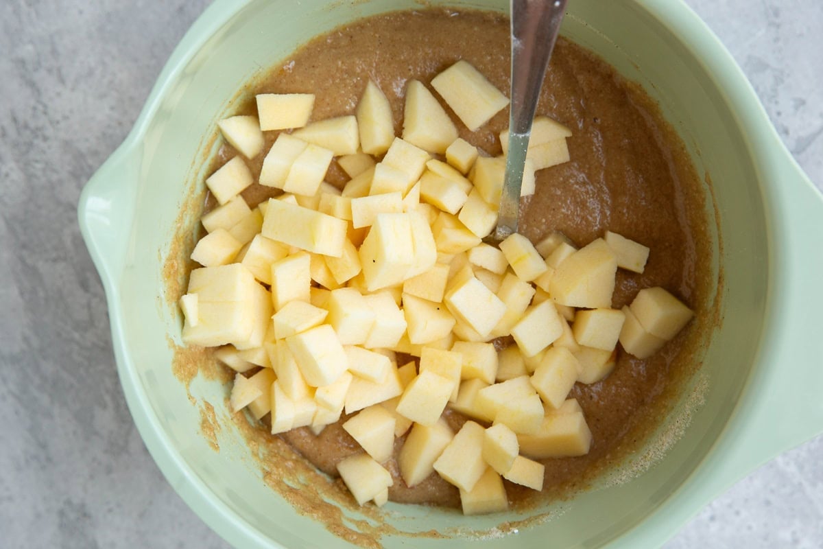 Mixing bowl full of apple bread batter with apple chunks on top, ready to be mixed in.