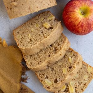Loaf of apple bread cut into slices with two fresh apples to the side.