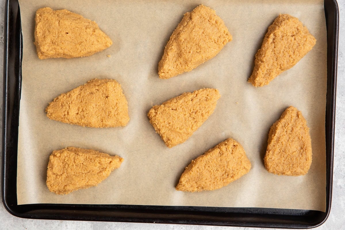 Baking sheet lined with parchment paper with 8 triangles of pumpkin scone dough on top.