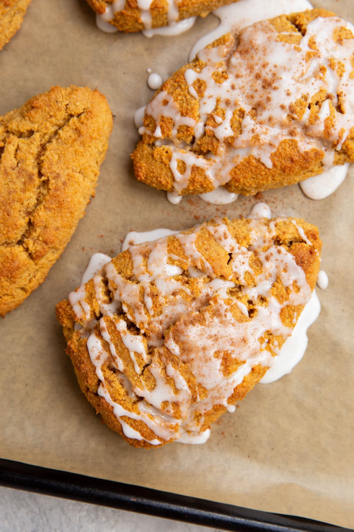 Almond Flour Pumpkin Scones drizzled with glaze and sprinkled with pumpkin pie spice on a baking sheet.