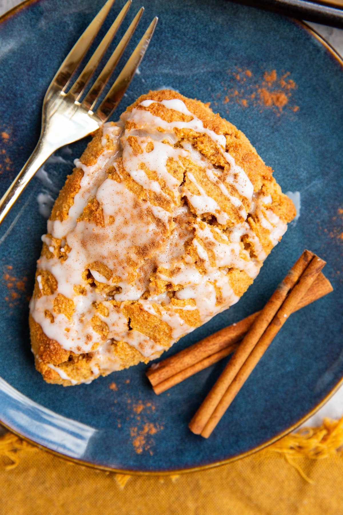 Pumpkin scone on a blue plate with a gold fork and cinnamon sticks to the side.