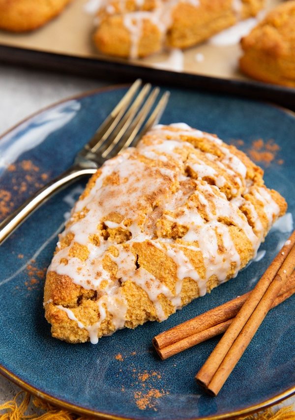 pumpkin scone on a blue plate with cinnamon sticks to the side.