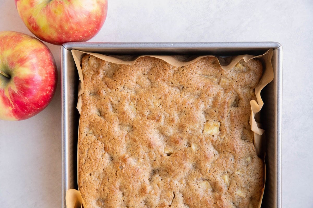 Applesauce cake in a baking pan, fresh out of the oven with two fresh apples to the side.
