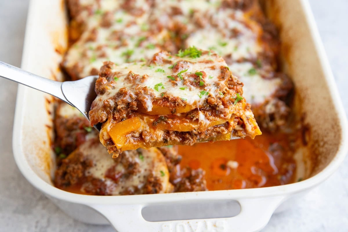 Casserole dish full of butternut squash lasagna and a spatula pulling out a slice of lasagna