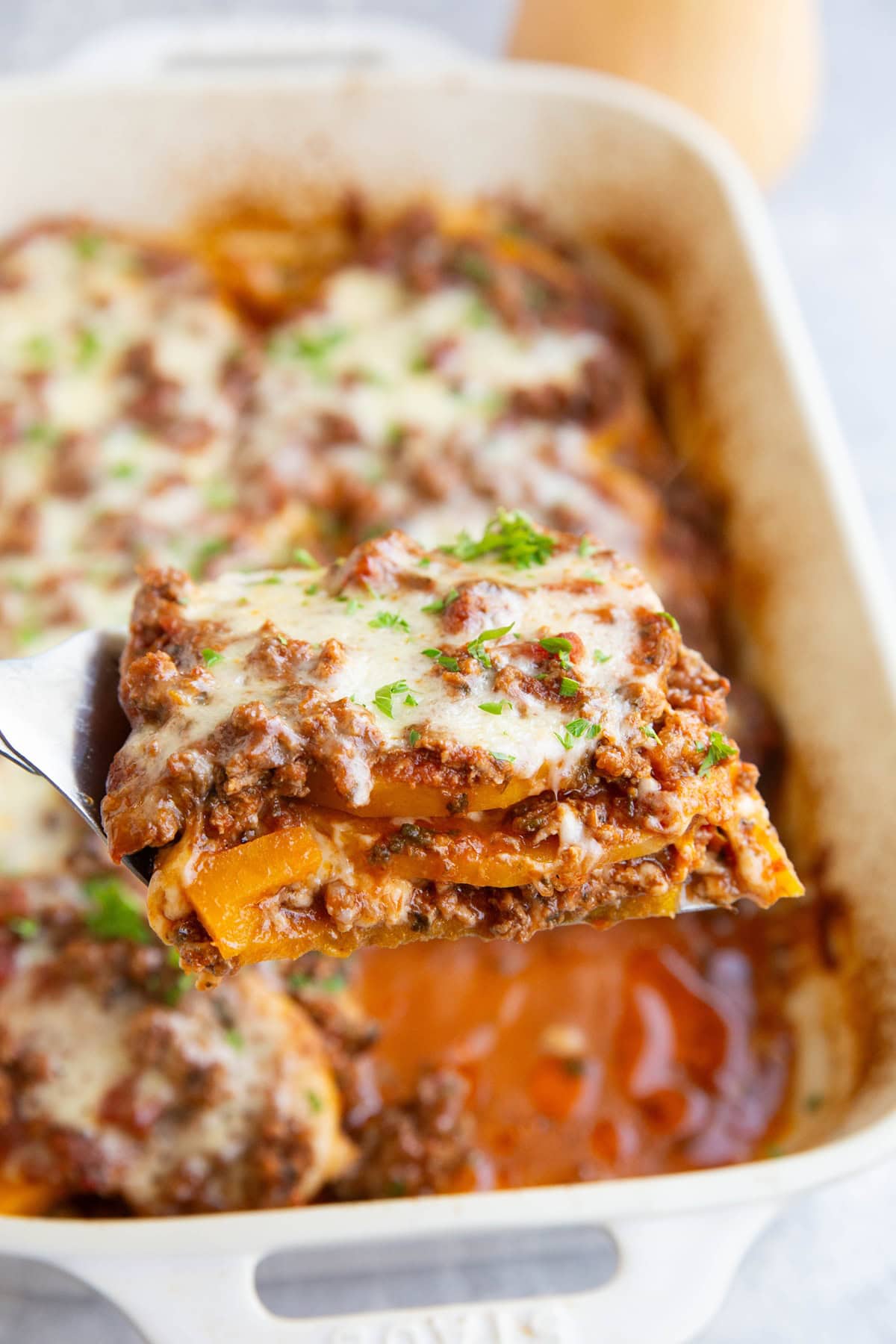 Casserole dish of butternut squash lasagna with a slice being pulled out with a spatula.