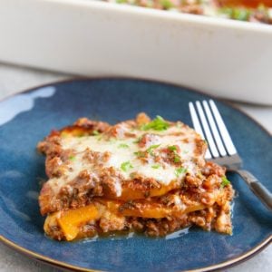 Slice of butternut squash lasagna on a blue plate with the rest of the pan of lasagna in the background.