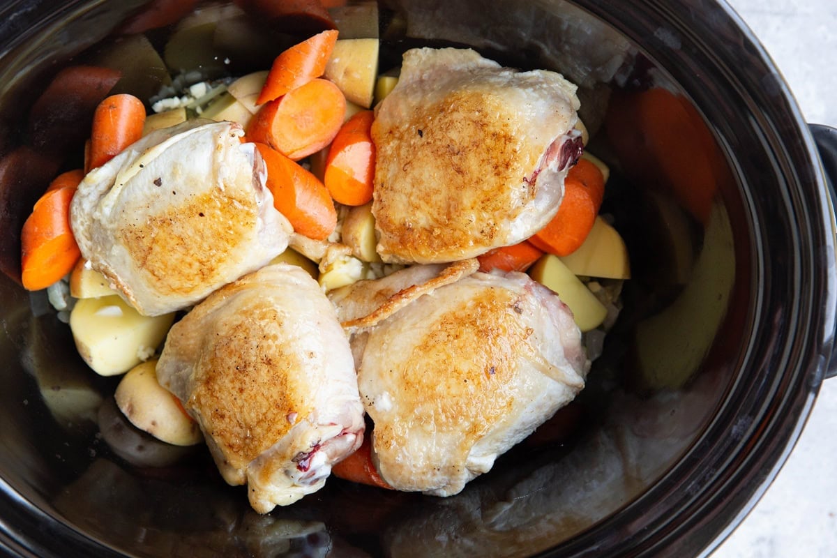 Chopped carrots, potatoes, onions, and seared chicken thighs in a rock pot.
