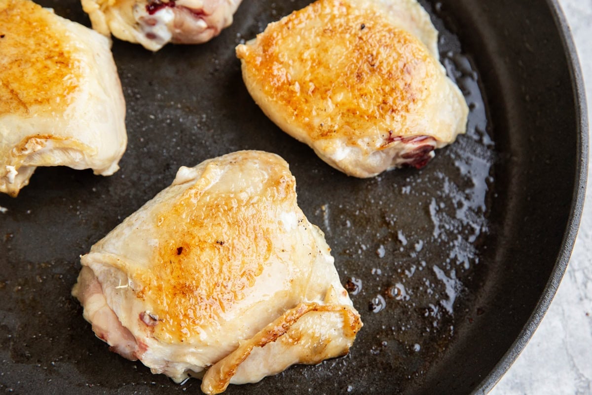 Chicken thighs searing in a skillet.