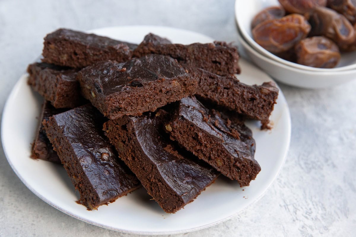 plate full of date brownies with a bowl of dates in the background.