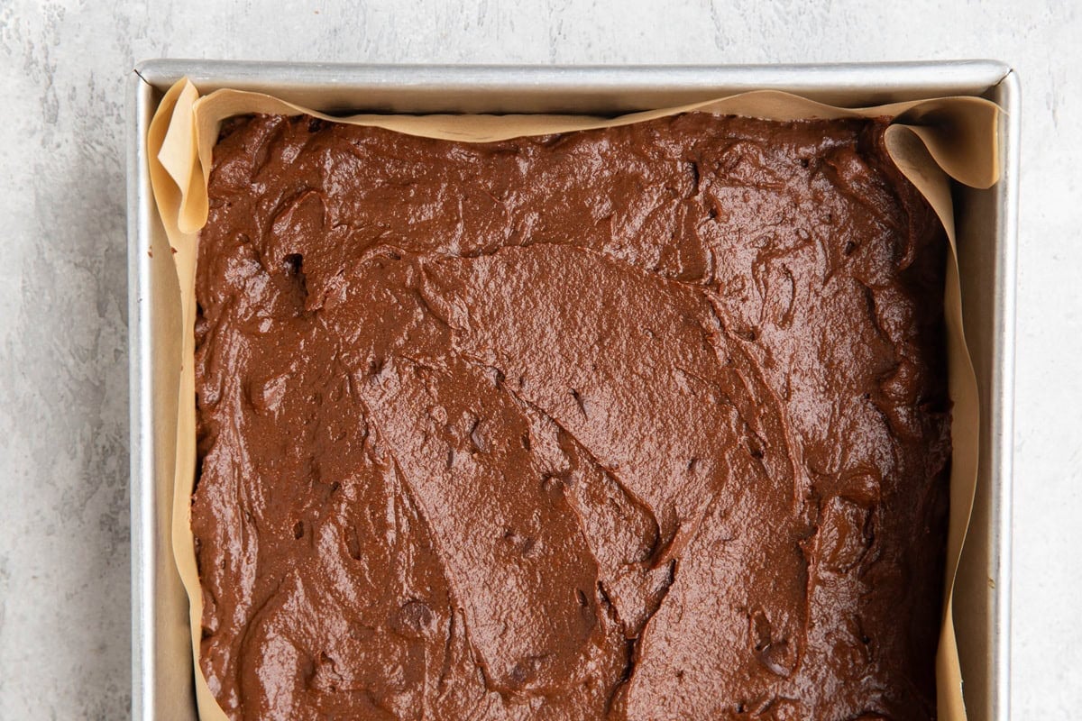 Brownie batter in a baking dish lined with parchment paper.