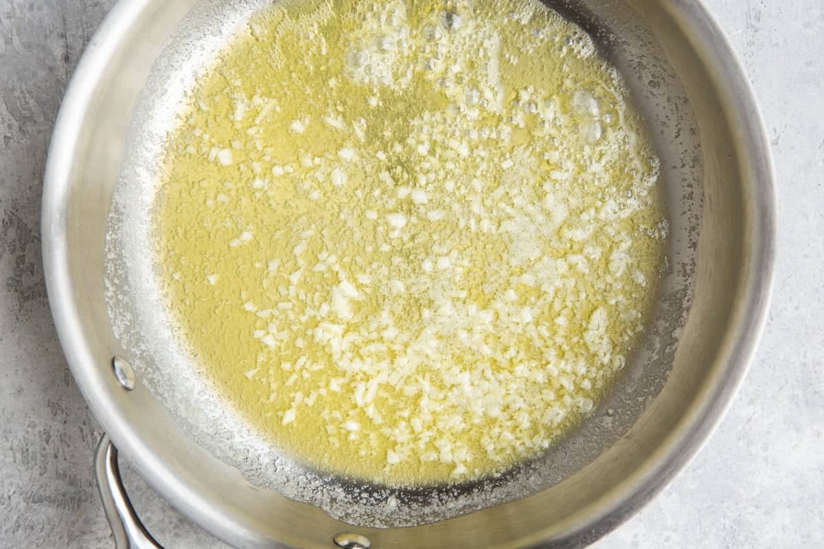 Stainless steel skillet of garlic sautéing in butter.
