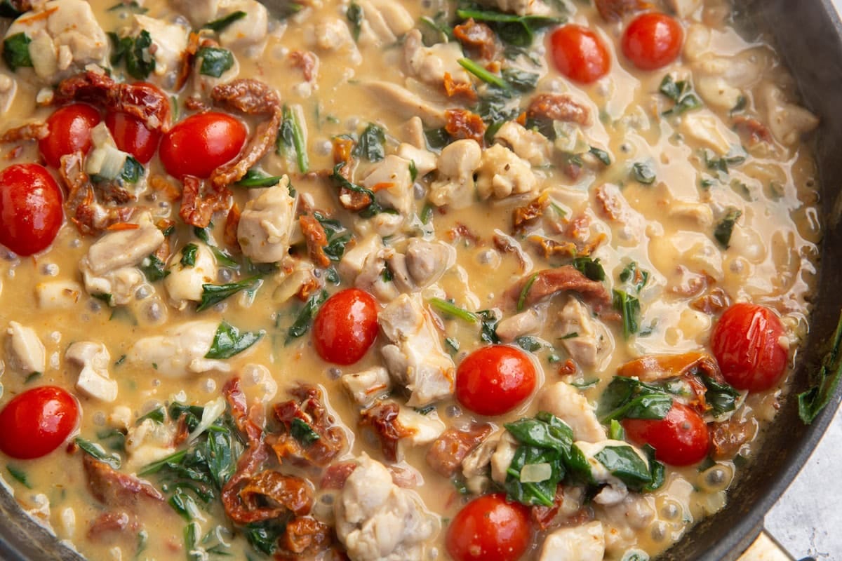 large skillet full of chicken smothered in a creamy sun-dried tomato sauce with cherry tomatoes and baby spinach. Ready to use on pasta.