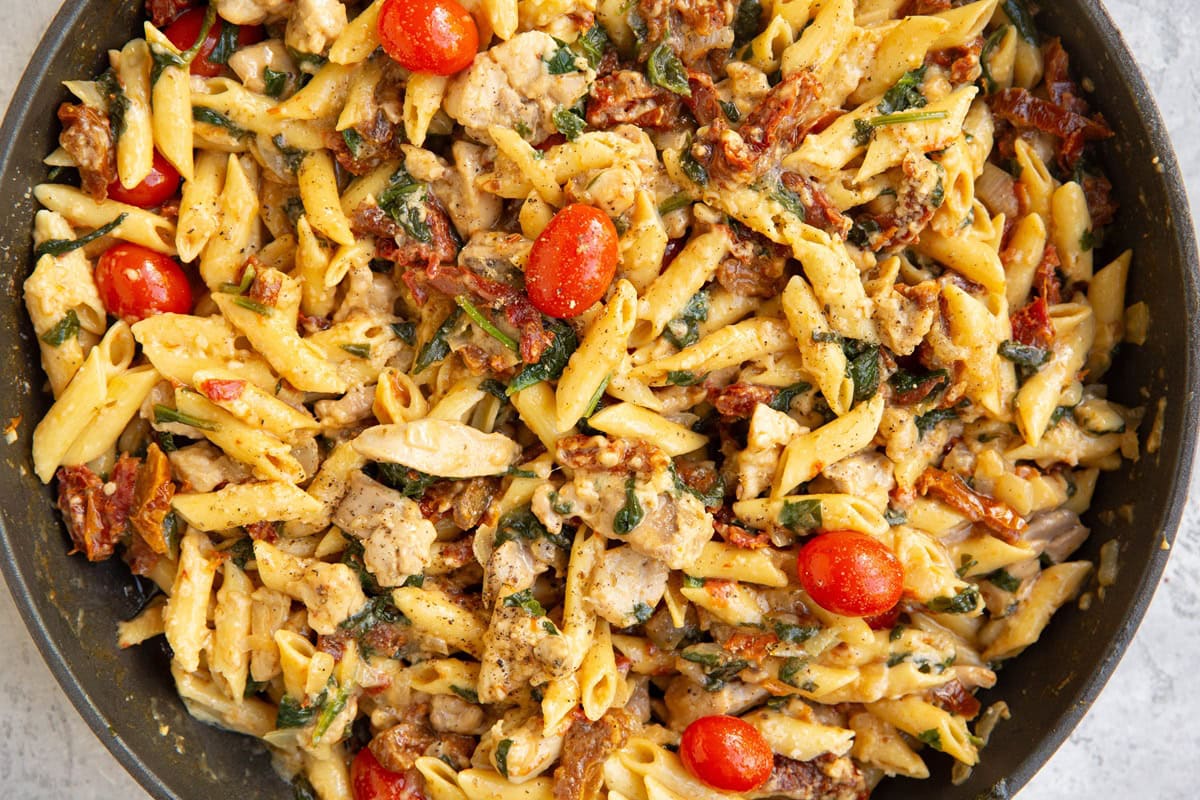 Chicken pasta in a skillet with tomatoes and spinach.