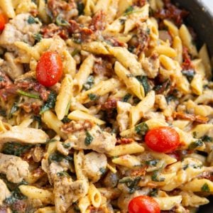 Chicken penne pasta in a skillet with tomatoes and creamy sauce.