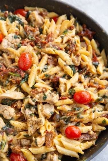 Chicken penne pasta in a skillet with tomatoes and creamy sauce.