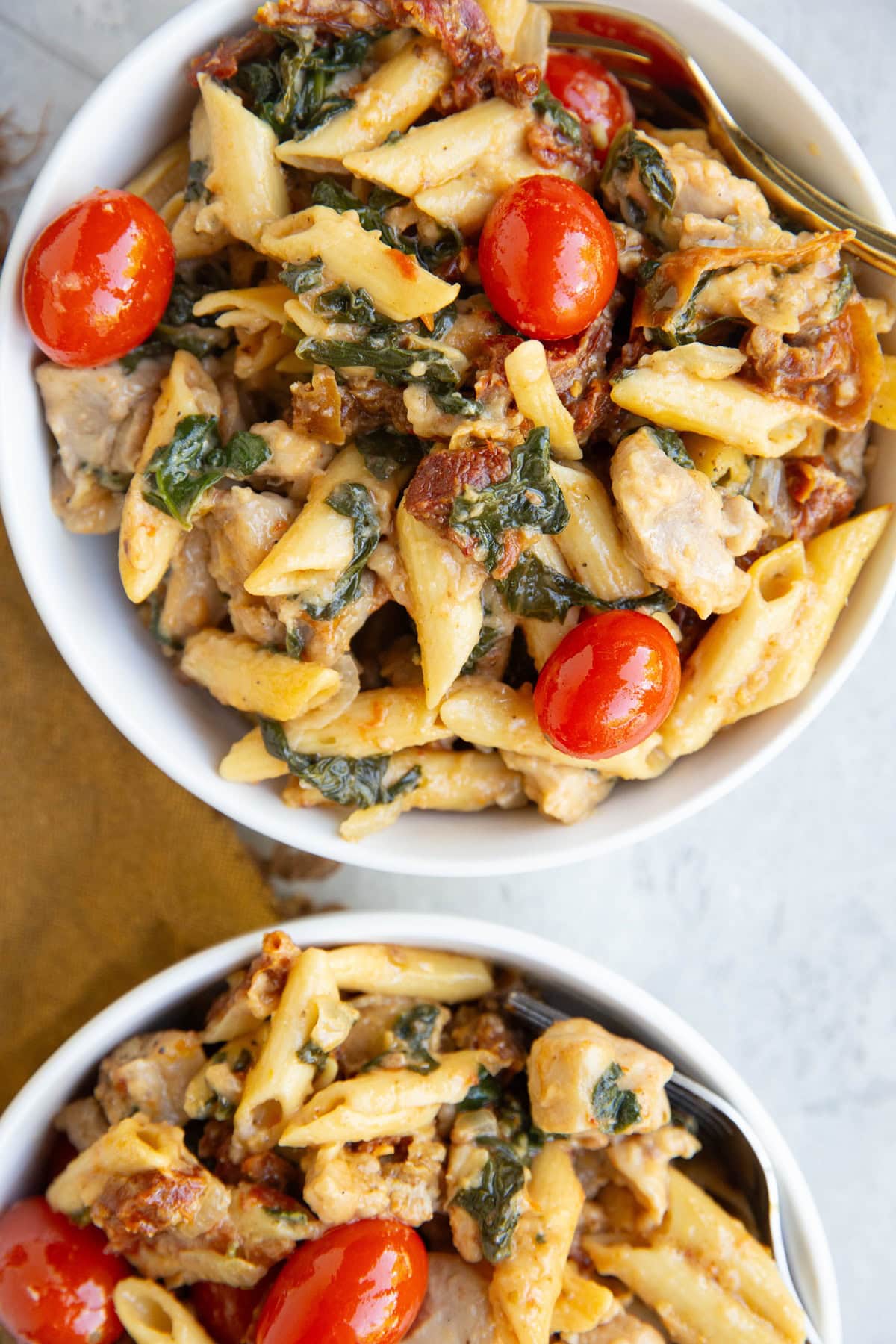 Two bowls of chicken pasta with sun-dried tomatoes, cherry tomatoes, spinach, and more. Ready to eat.