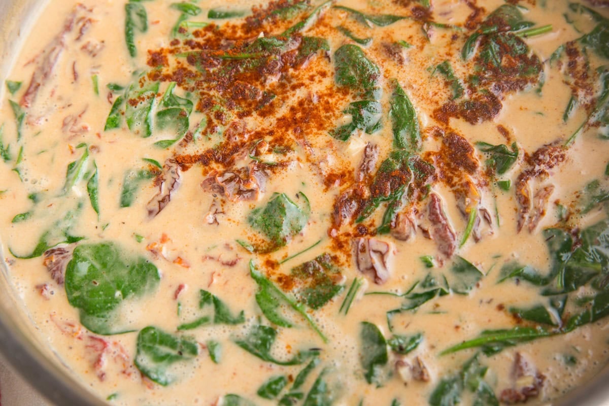 Sun-dried tomato sauce with spinach and paprika cooking in a stainless steel skillet.