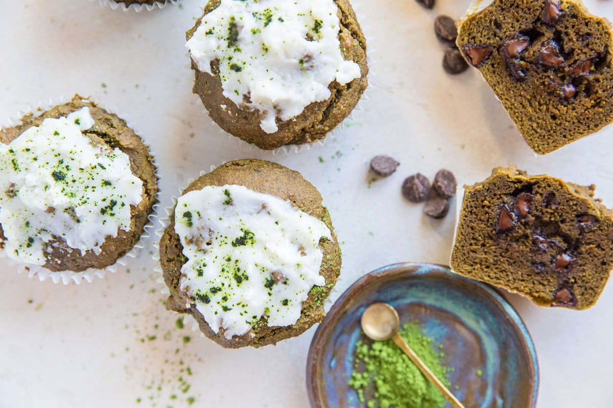 A matcha muffin cut in half to expose chocolate chips on the inside and more matcha muffins to the side.