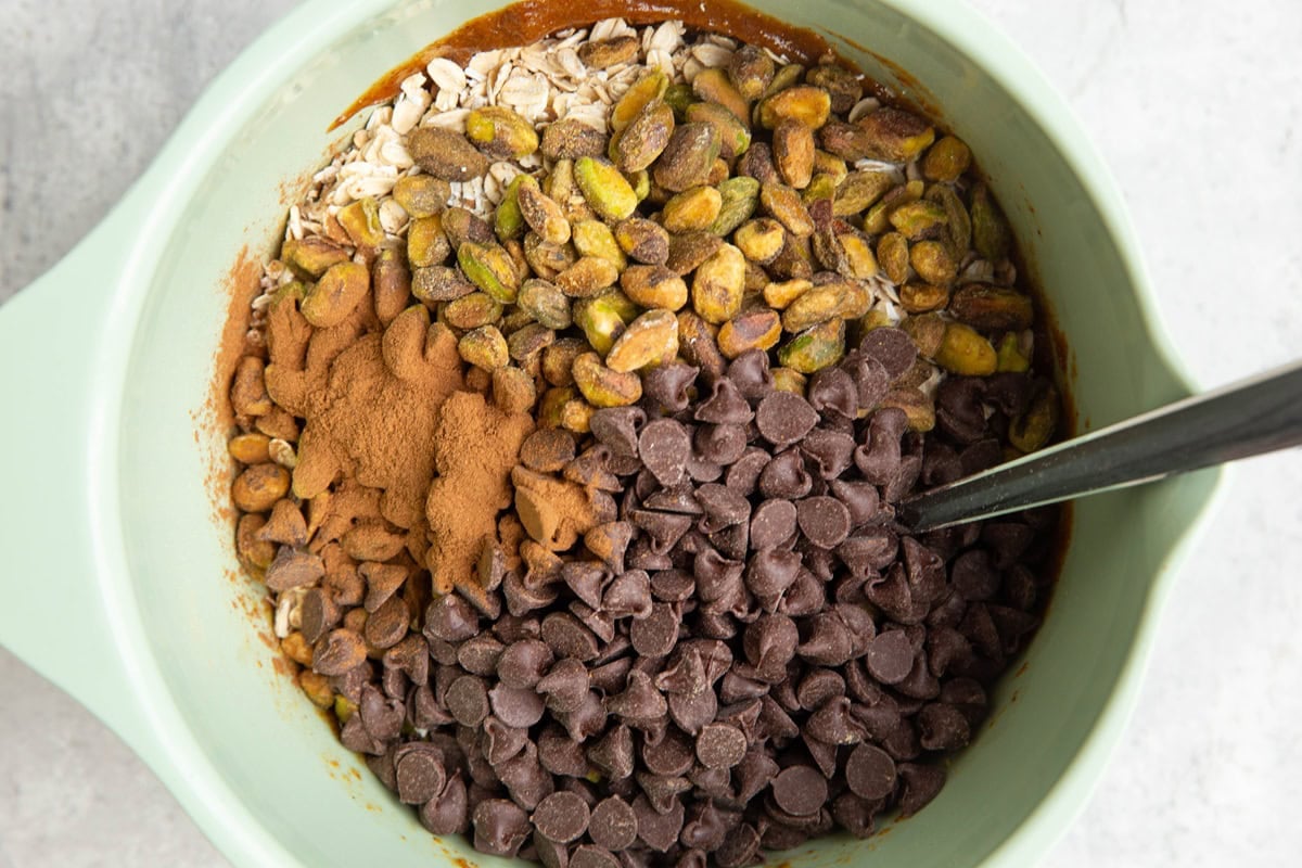 Mixing bowl with oats, pistachios, chocolate chips, and cinnamon to be mixed into wet ingredients for cookie dough.