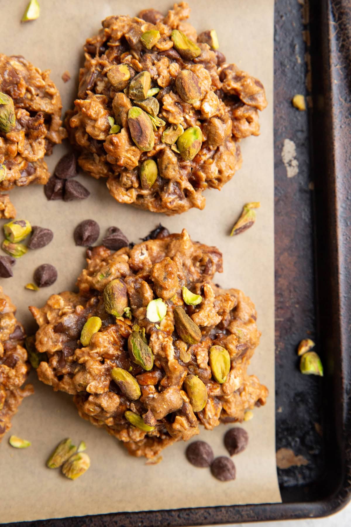 Baking sheet with pistachio cookies and chocolate chips and pistachios sprinkled all around.