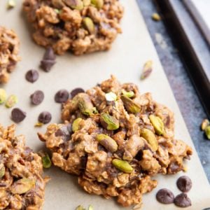 Baking sheet with pistachio cookies. Chocolate chips and chopped pistachios sprinkled around the cookies.