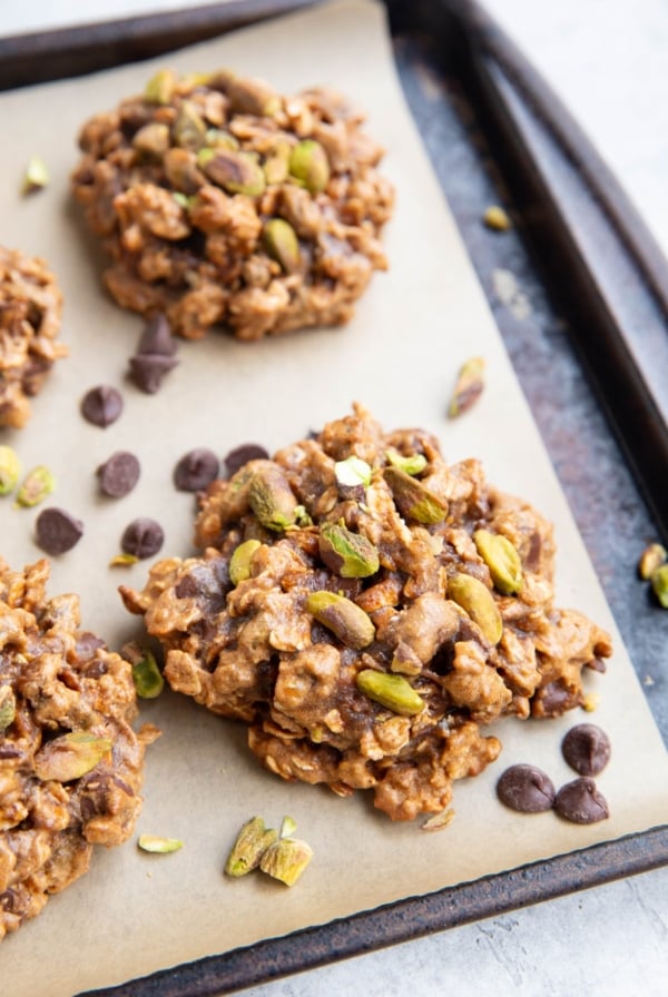 Baking sheet with pistachio cookies. Chocolate chips and chopped pistachios sprinkled around the cookies.