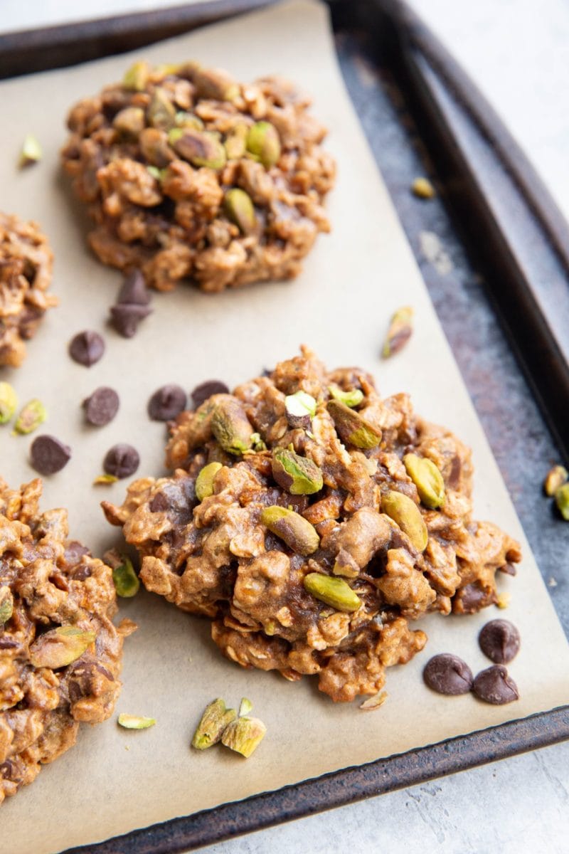 Baking sheet with pistachio cookies. Chocolate chips and chopped pistachios sprinkled around the cookies.