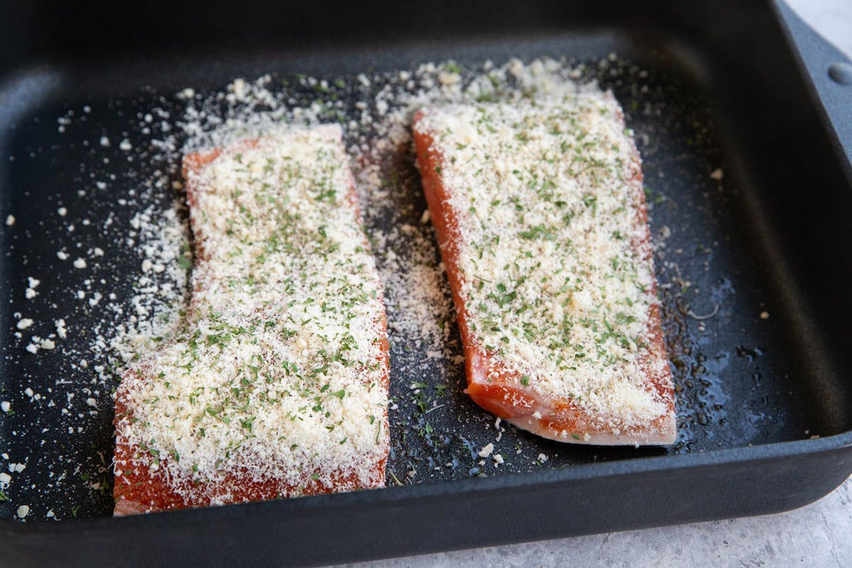 Baking dish with raw salmon inside with parmesan cheese sprinkled on top