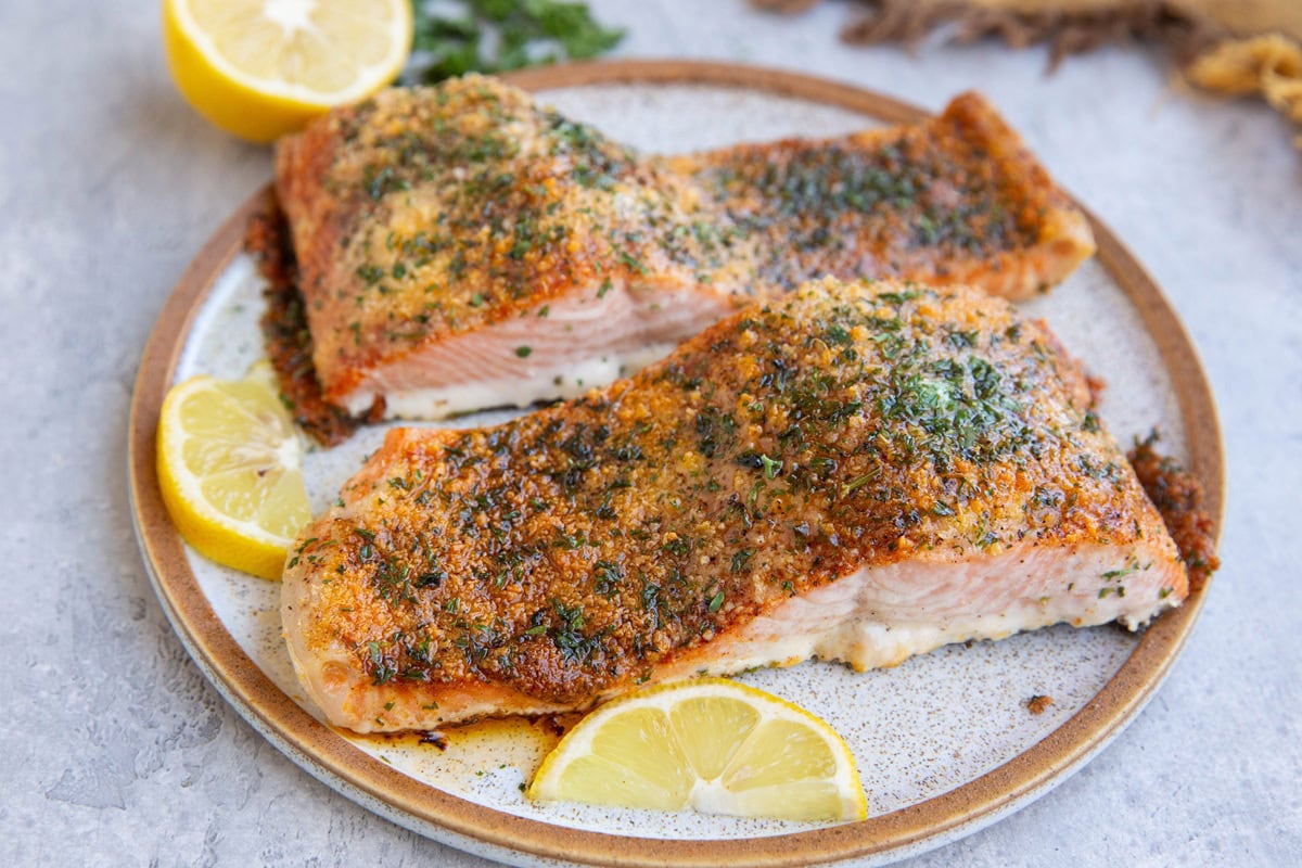 parmesan crusted salmon filets on a plate with lemon wedges and a fresh lemon in the background.