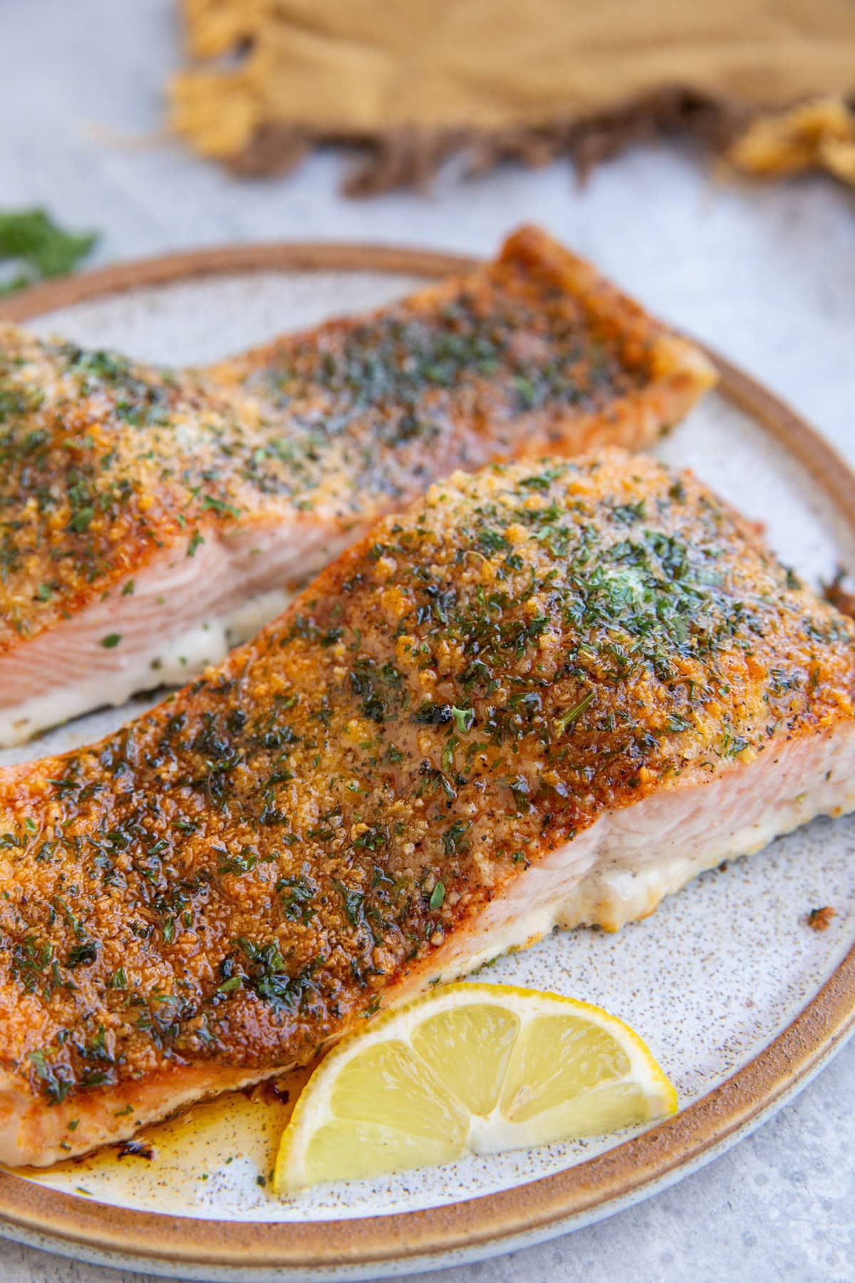 Two crusted salmon filets on a plate with sliced lemon wedges and a cloth napkin in the background.