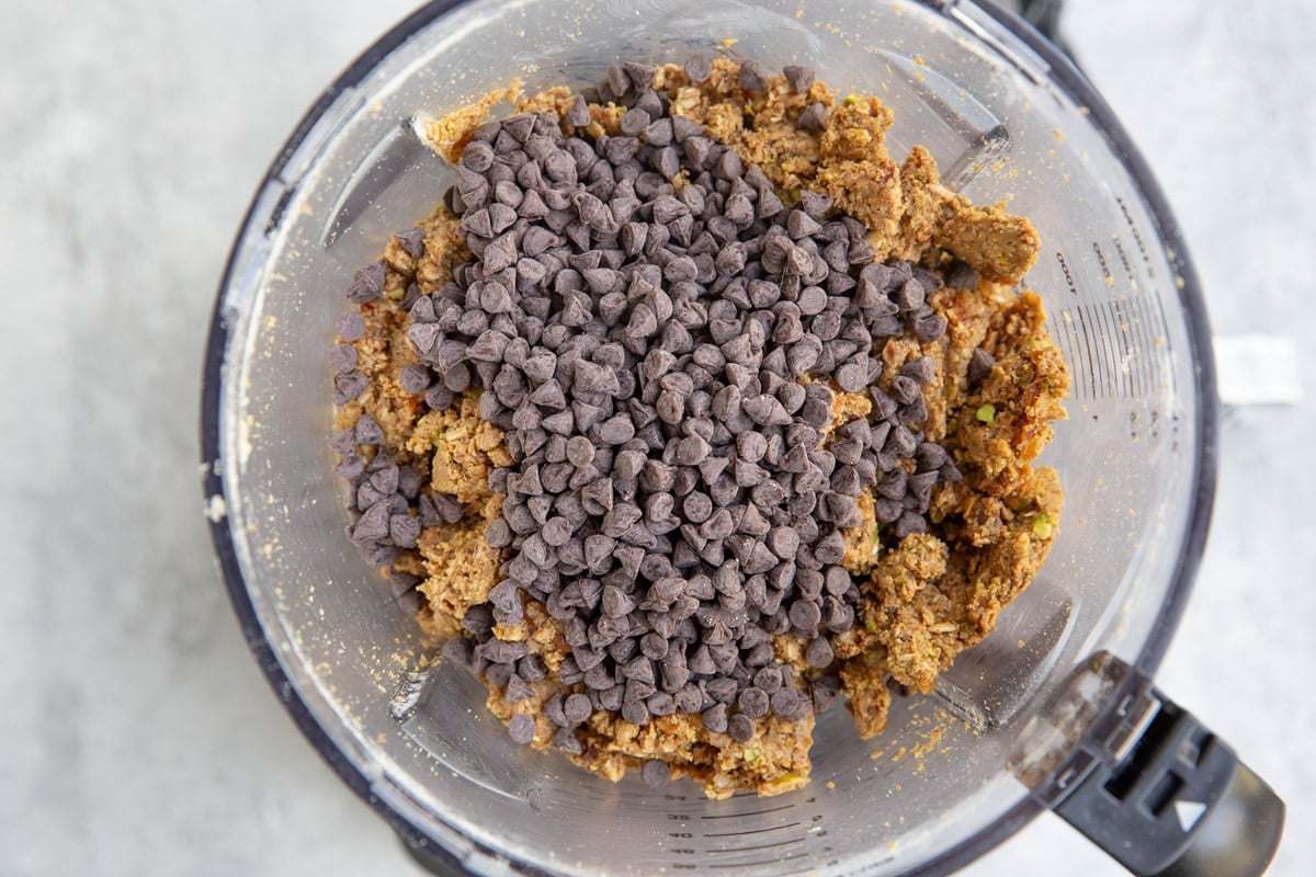 Pistachio protein ball mixture with mini chocolate chips on top in a food processor, waiting to be mixed in.