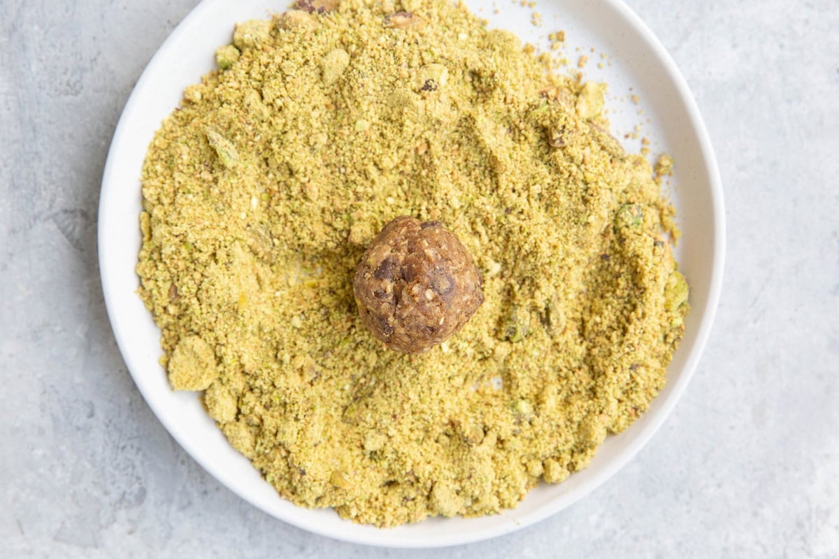 Small plate with ground up pistachios and an energy ball sitting in the center, to be coated with pistachio dust.