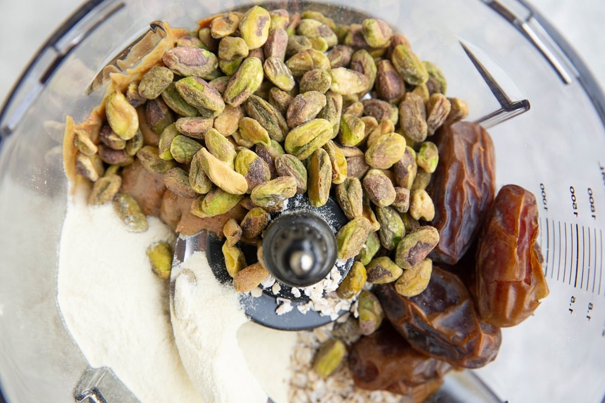 Food processor with oats, pitted dates, pistachios, protein powder, cinnamon and salt to make pistachio protein balls.