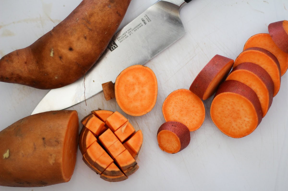 Sweet potato cut into slices, then chopped into cubes on a cutting board.