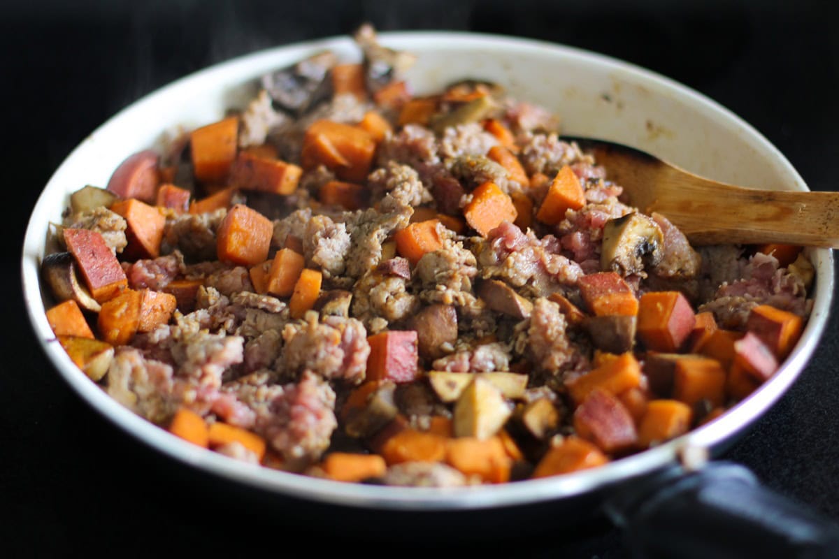 sweet potato, mushrooms, garlic, and sausage cooking in a skillet