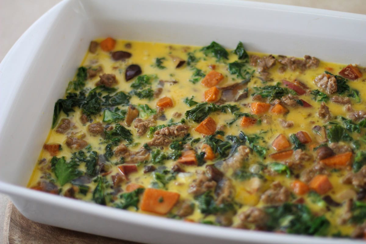 Sausage, kale and sweet potato surrounded by beaten eggs in a casserole.