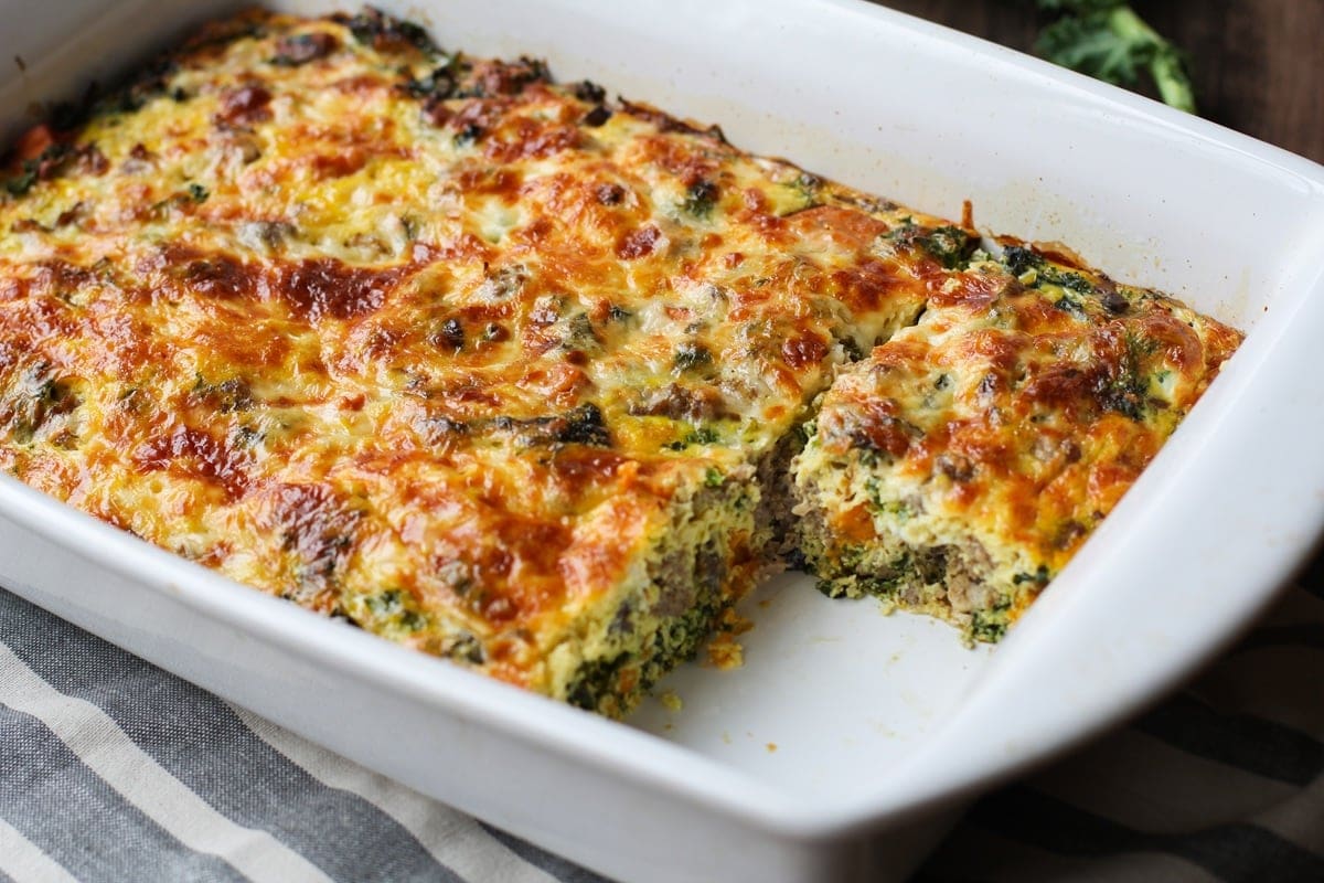 Casserole dish full of sausage, sweet potato and kale breakfast casserole with a slice taken out.